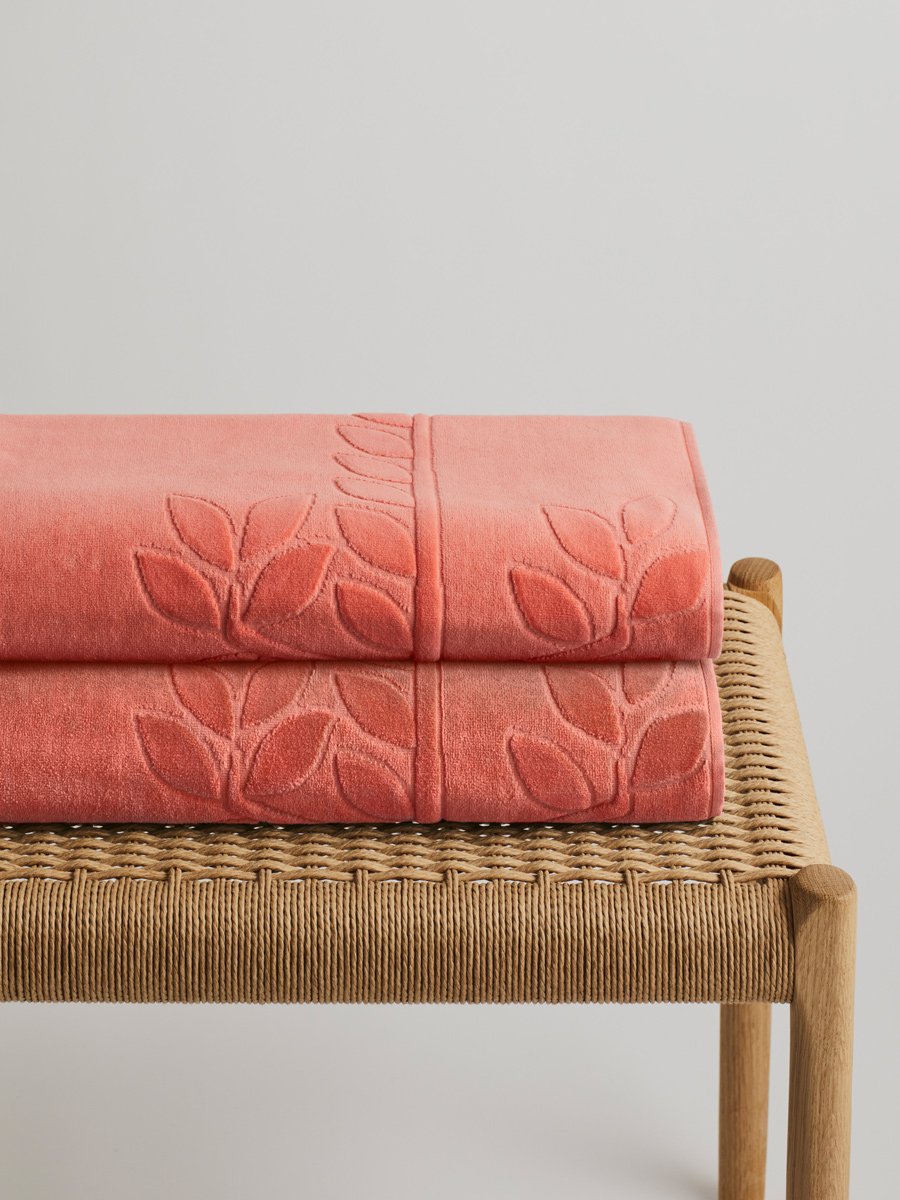 Two 'Red Sea Coral' beach towels folded on a wooden bench. The towels feature a subtle leaf pattern. - {{Red Sea Coral}}