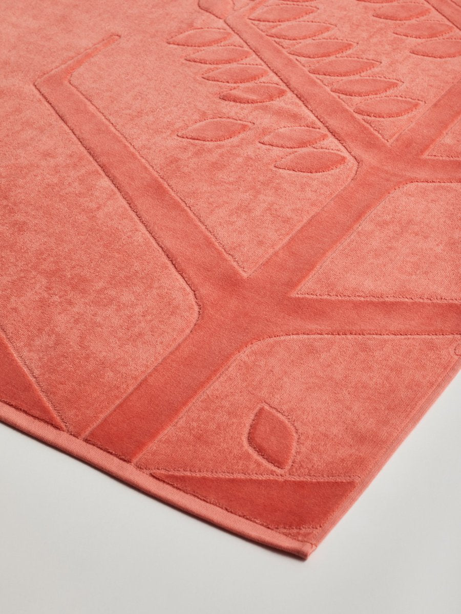 Close-up of a 'Red Sea Coral' beach towel with a textured and embossed Four Seasons logo design. - {{Red Sea Coral}}