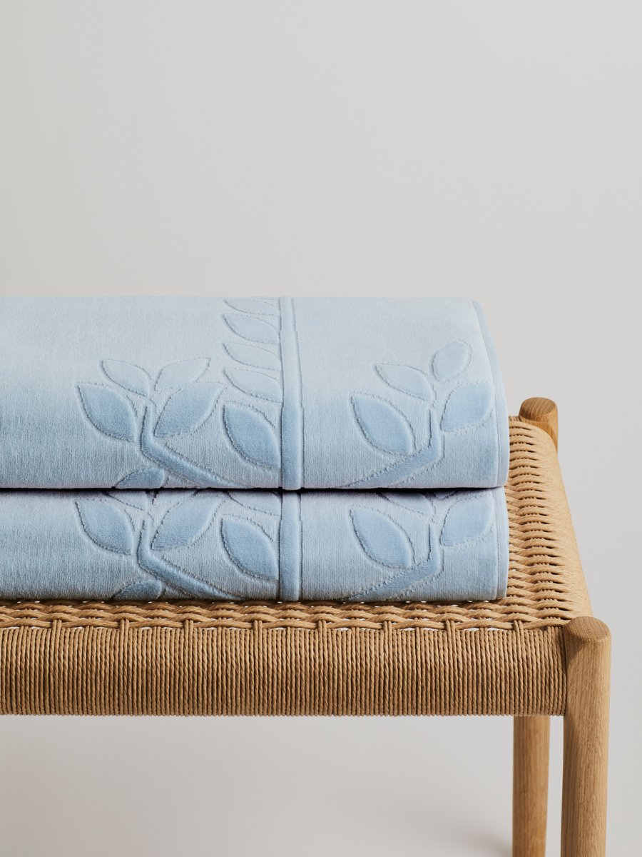 Two 'Maldivian Atoll' beach towels folded on a wooden bench. The towels feature a subtle leaf pattern. - {{Maldivian Atoll}}