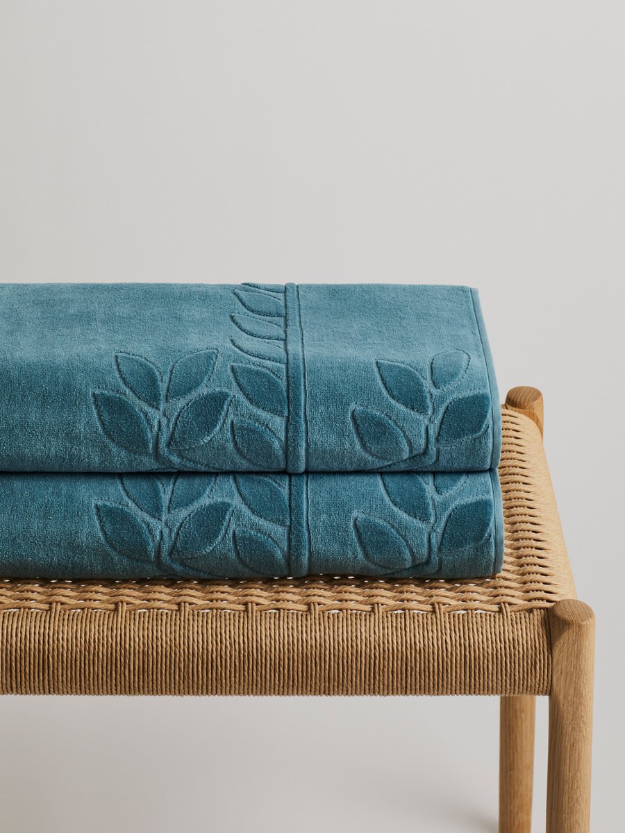 Two 'Polynesian Lagoon' beach towels folded on a wooden bench. The towels feature a subtle leaf pattern. - {{Polynesian Lagoon}}
