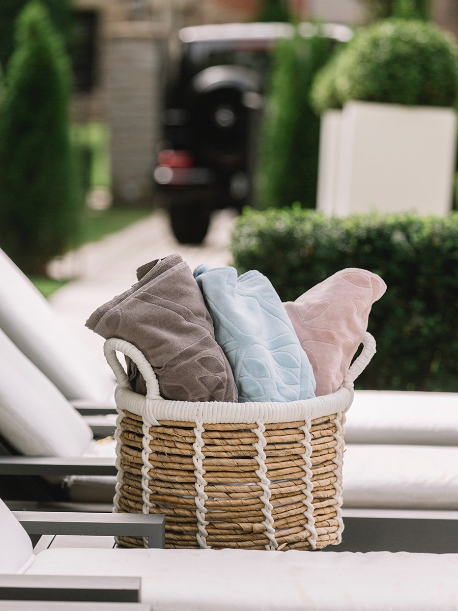 Three folded beach towels in different colors are displayed in a basket next to a poolside lounge chair. - {{Maldivian Atoll}}