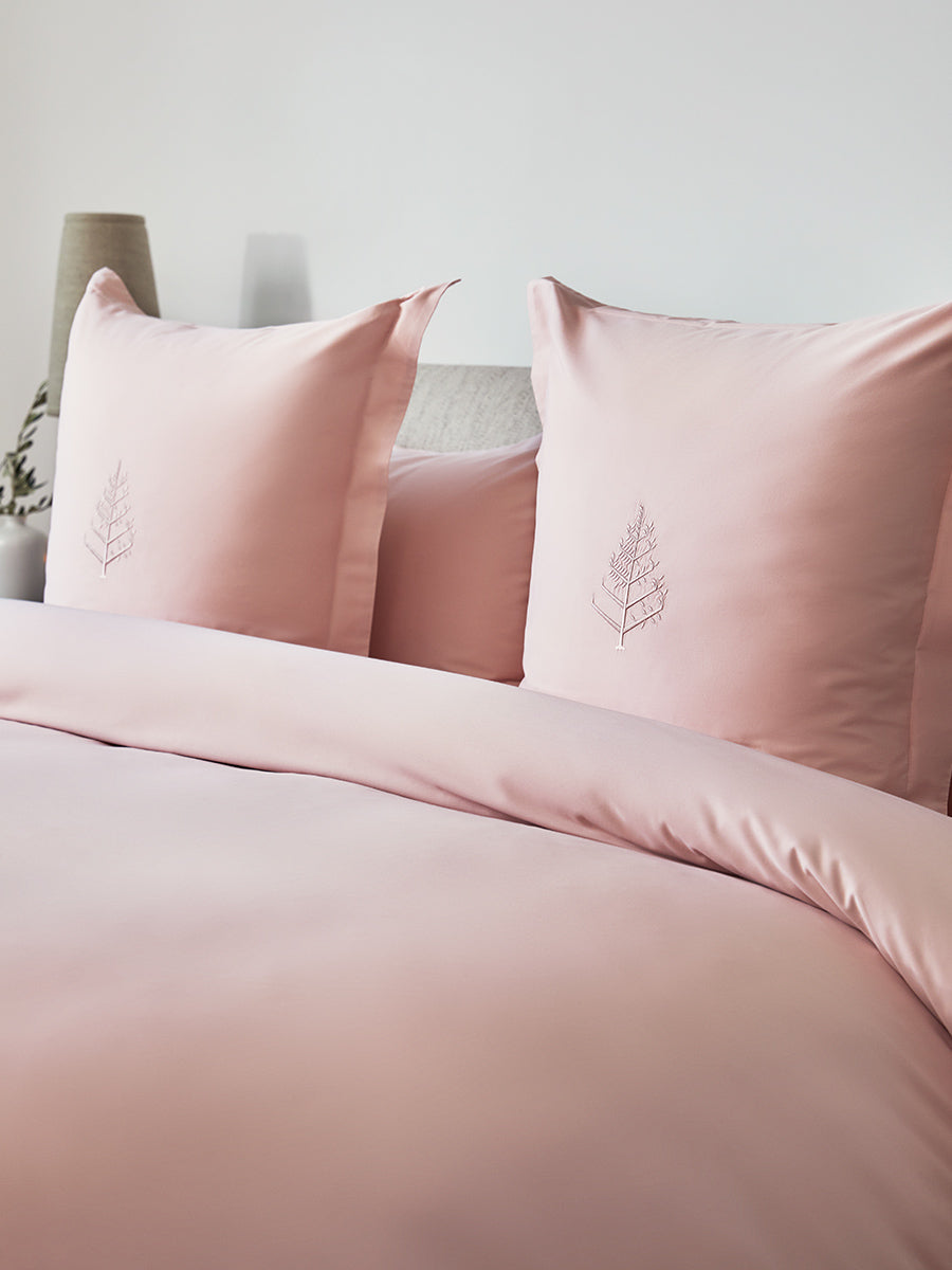 Close-up of Kyoto Blush duvet cover set; two bordered shams featuring tone-on-tone logo store; soft-focus beige lamp in background. {{Kyoto Blush}}