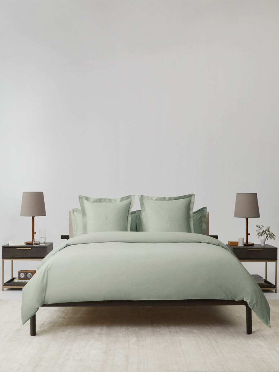 Bed dressed in a Florentine Sage duvet cover set; bordered shams with tone-on-tone logo store; minimalist nightstands and lamps. {{Florentine Sage}}