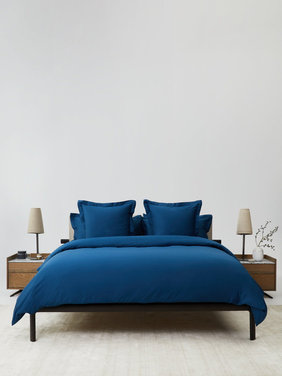 Bed dressed in a Riviera Navy duvet cover set; bordered shams with tone-on-tone logo store; minimalist nightstands and lamps. {{Riviera Navy}}