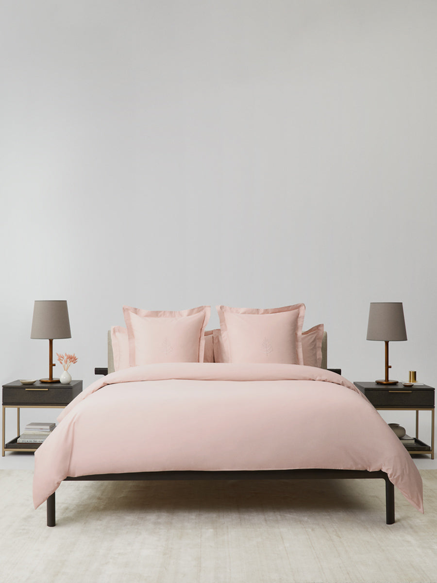 Bed dressed in a Kyoto Blush duvet cover set; bordered shams with tone-on-tone logo store; minimalist nightstands and lamps. {{Kyoto Blush}}