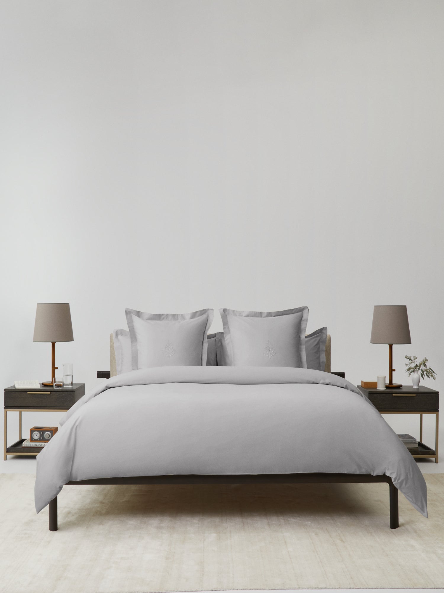 Front view of bed dressed in Turkish Silver duvet set with matching pillow shams featuring store logo, flanked by two nightstands with lamps. {{Turkish Silver}}