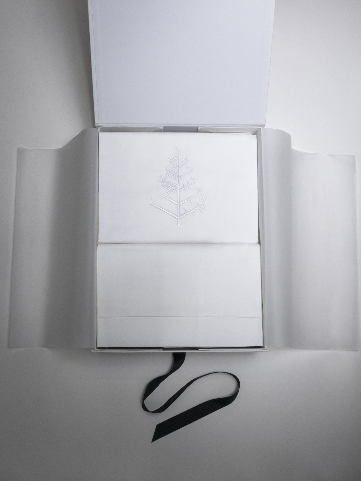 Open presentation box with folded white duvet cover set; top piece features tone-on-tone logo store embroidery and a black ribbon. {{Hampshire Charcoal}}