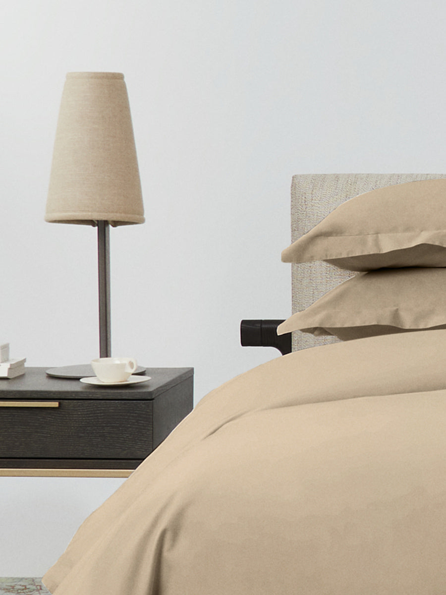 Side view of bed dressed in Egyptian Camel duvet set with matching pillow shams beside a nightstand and lamp. {{Egyptian Camel}}