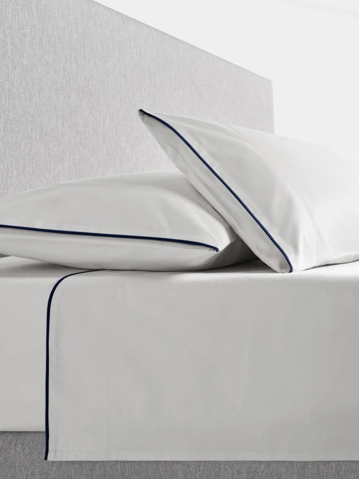Sycamore Sheet Set in Signature White —flat and fitted sheet with modern piped hem, styled on bed with matching pillowcases. - {{Signature White}}
