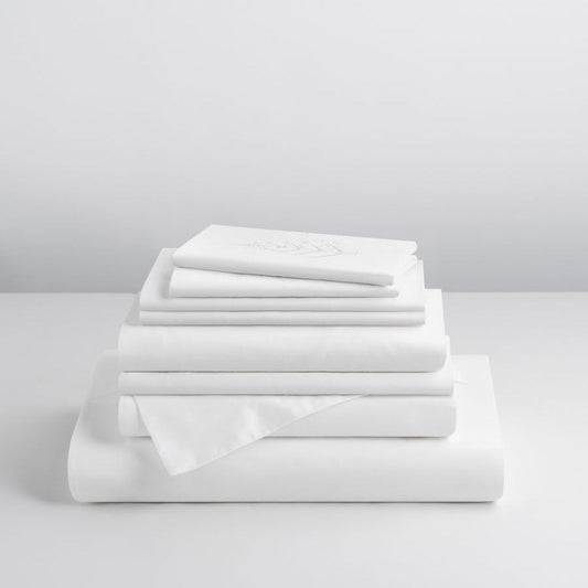 Signature Hotel Linen Set in Signature White stacked on a table—Supima cotton fitted sheet, flat sheet, pillowcases, duvet cover, pillow shams, and Euro shams with store logo. {{Signature White}}