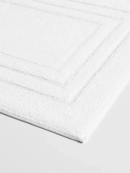 Close-up of a white bath mat with a subtle rectangular border pattern.