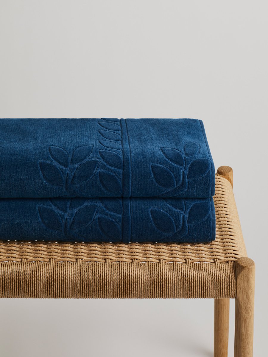 Two 'Riviera Navy' beach towels folded on a wooden bench. The towels feature a subtle leaf pattern. - {{Caribbean Seascape}}
