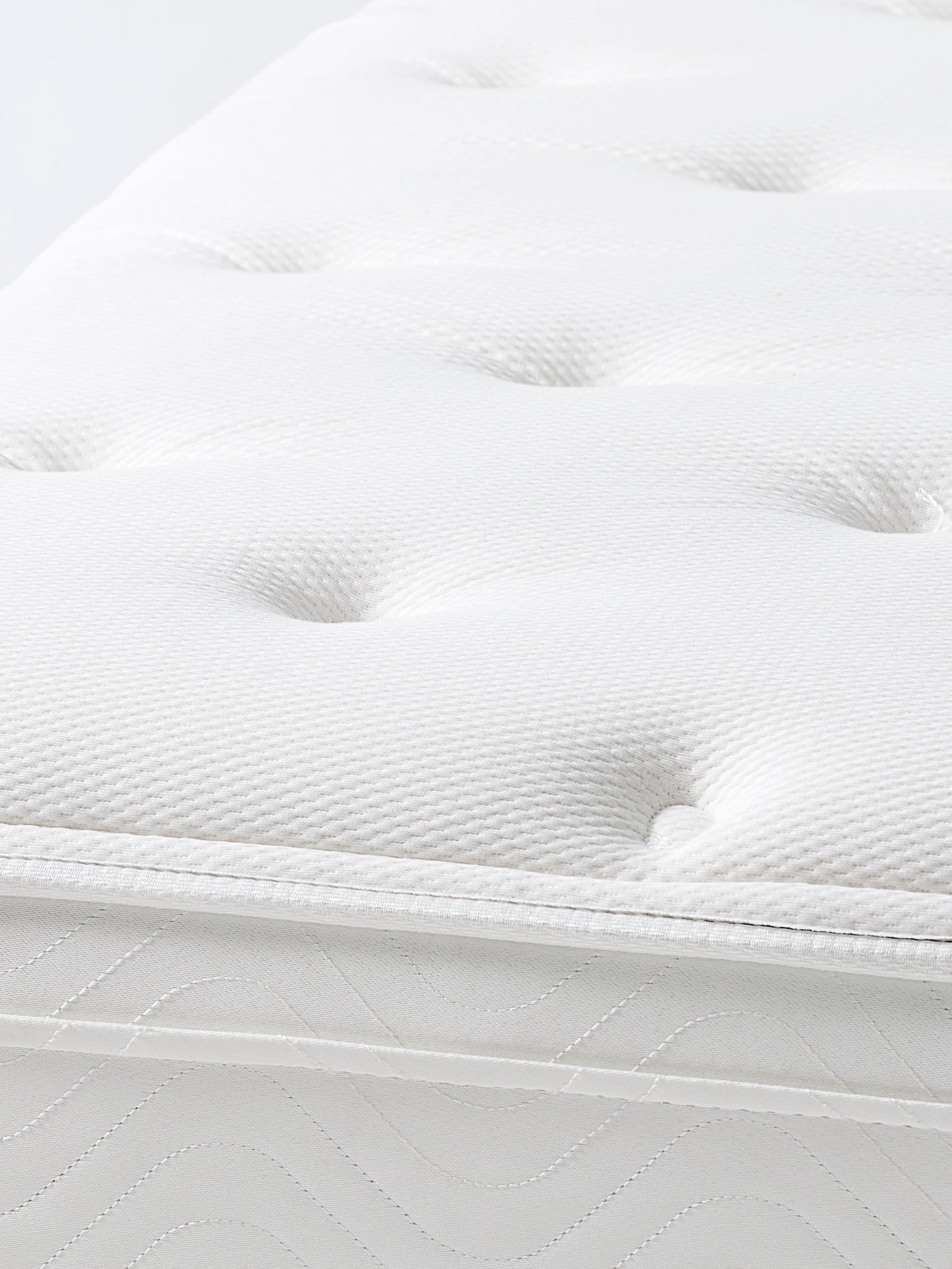 Close-up view of a white mattress with a quilted surface and a subtle pattern.