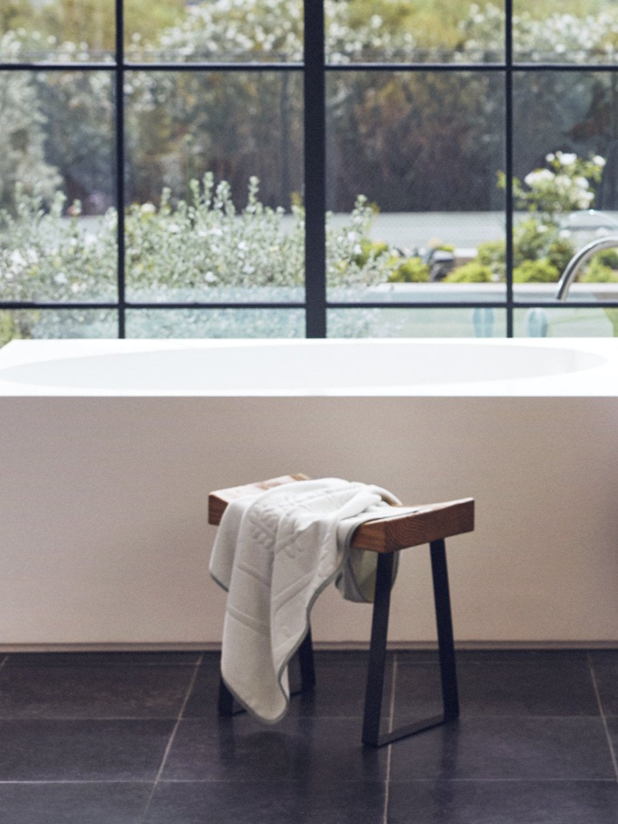 Baby towel in grey tones, placed on a wooden chair in a bright bathroom - {{Safari Sage / Mountain Grey}}