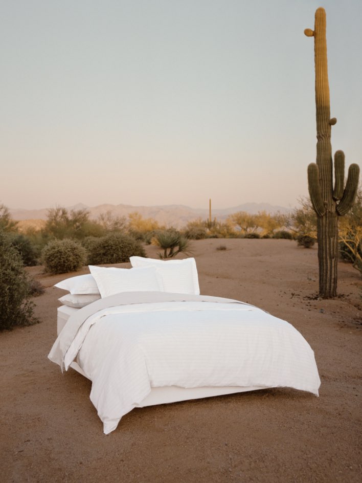 Bed dressed with white sheets and a duvet, with several pillows carefully arranged.