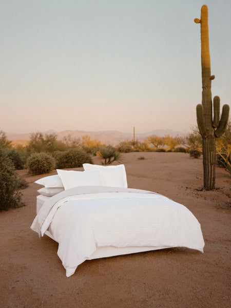 Bed dressed with white sheets and a duvet, with several pillows carefully arranged.