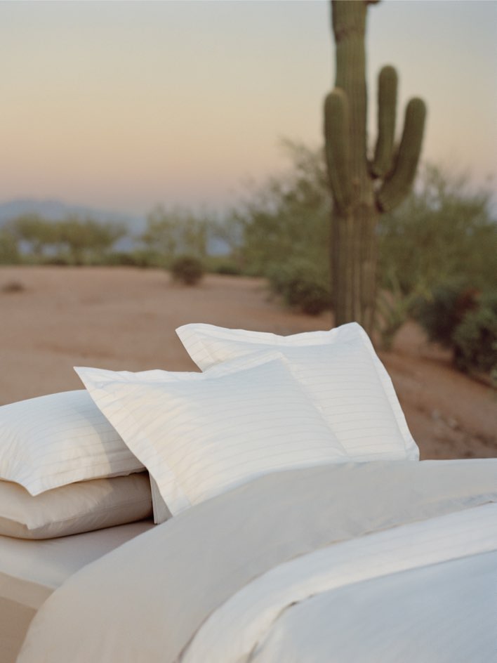 Bed dressed with white sheets and a duvet, with several pillows carefully arranged.