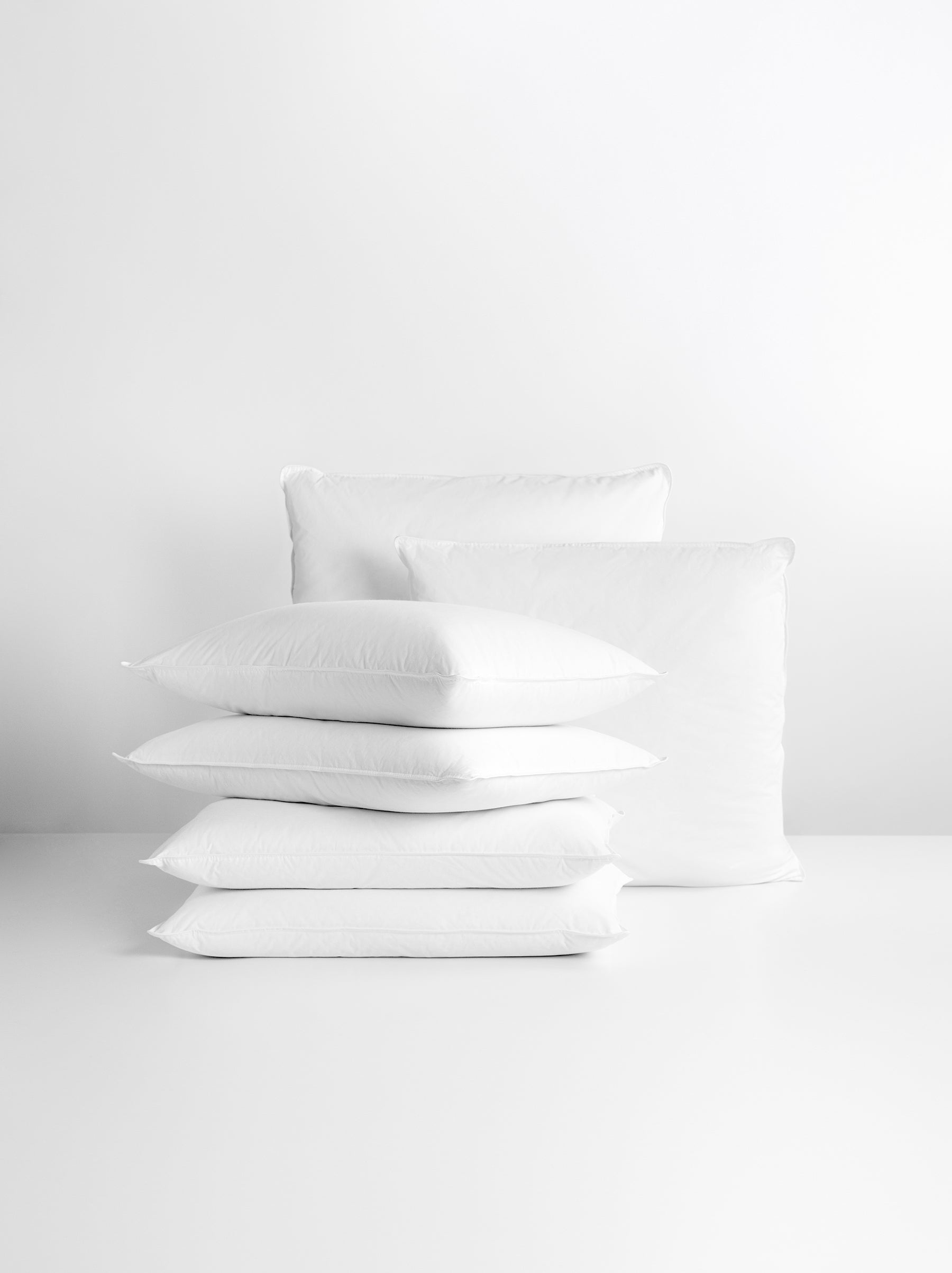 White pillow set. Several pillows are stacked on top of each other, and two larger pillows are propped up behind them.