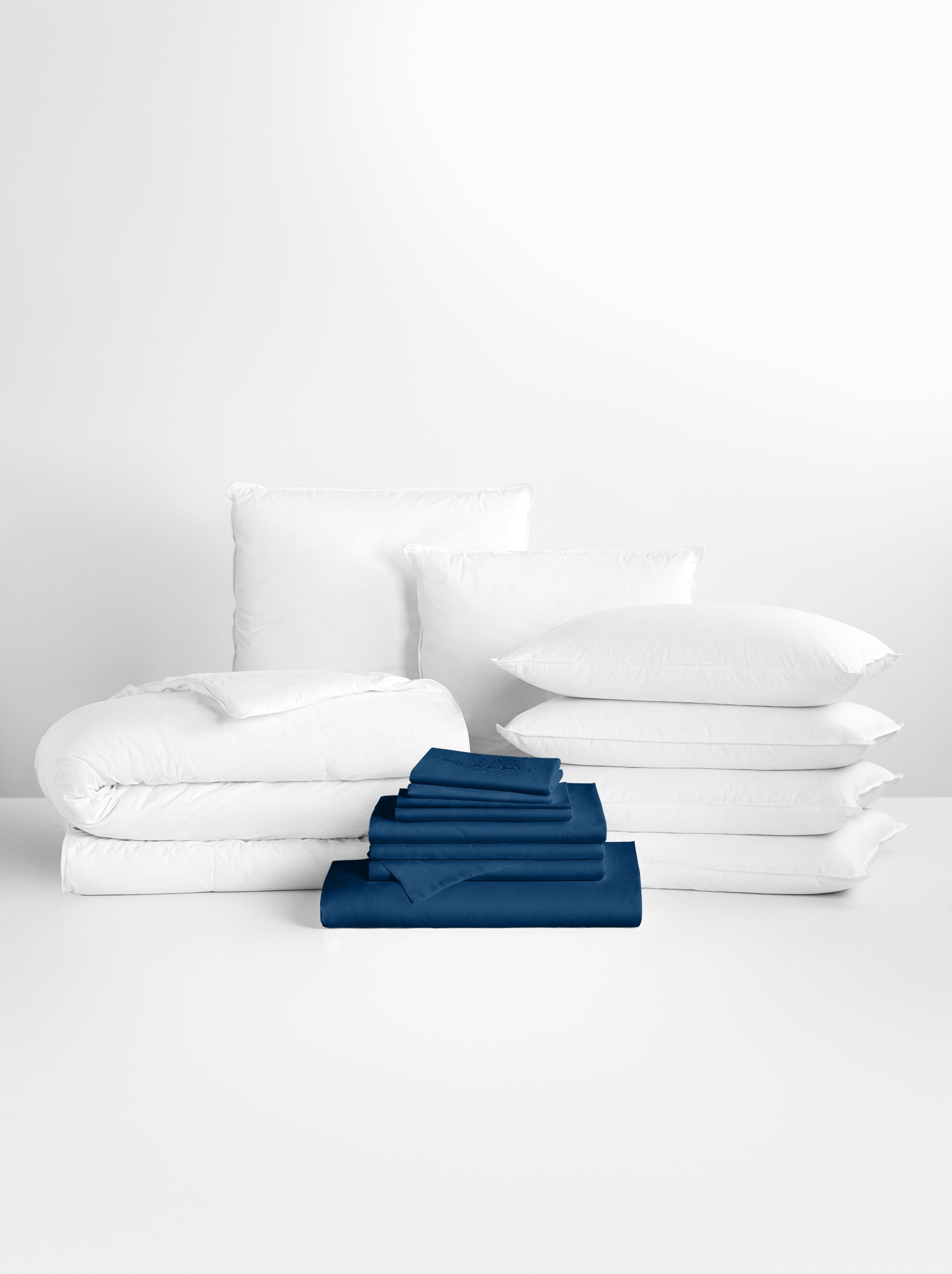 Riviera Navy-colored sheet set in the foreground, with stacked pillows and a neatly folded duvet in the background.