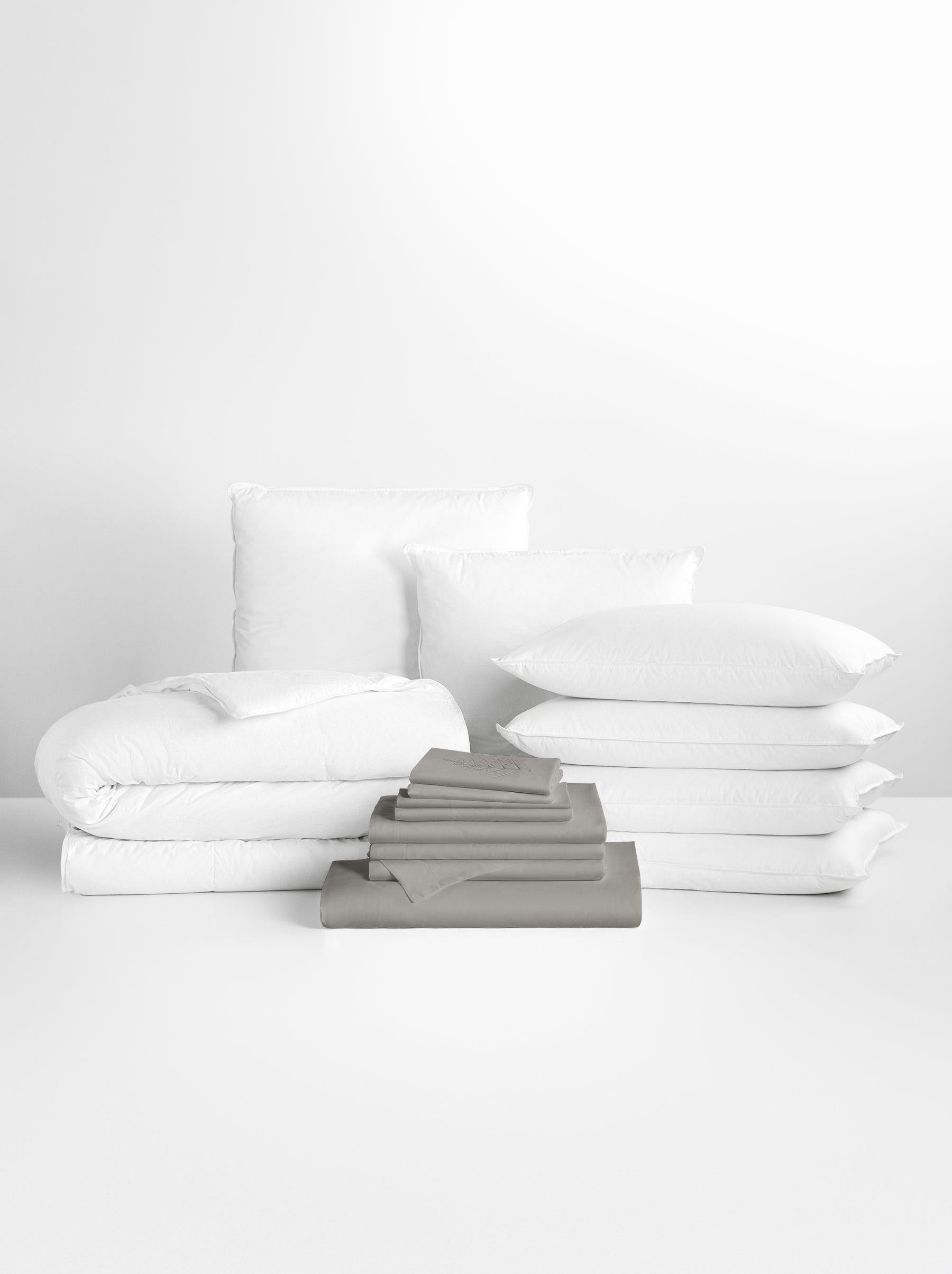 Spanish Slate-colored sheet set in the foreground, with stacked pillows and a neatly folded duvet in the background.