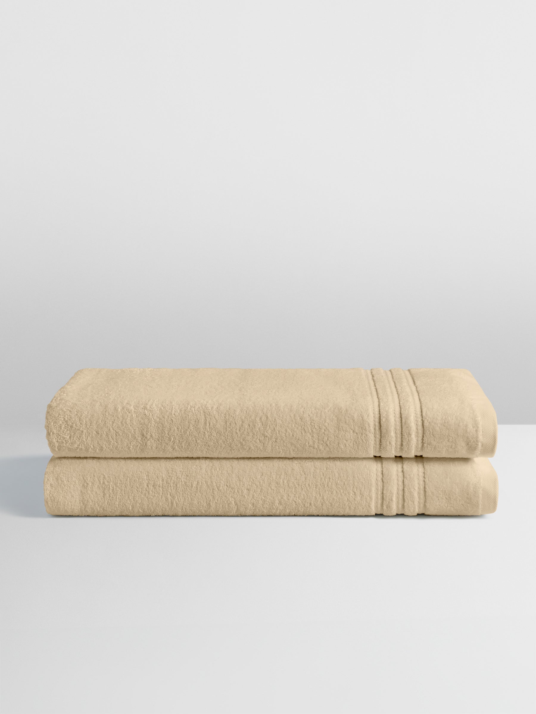 Two folded bath sheets in a warm, luxurious Egyptian Camel color, stacked neatly on a white surface.