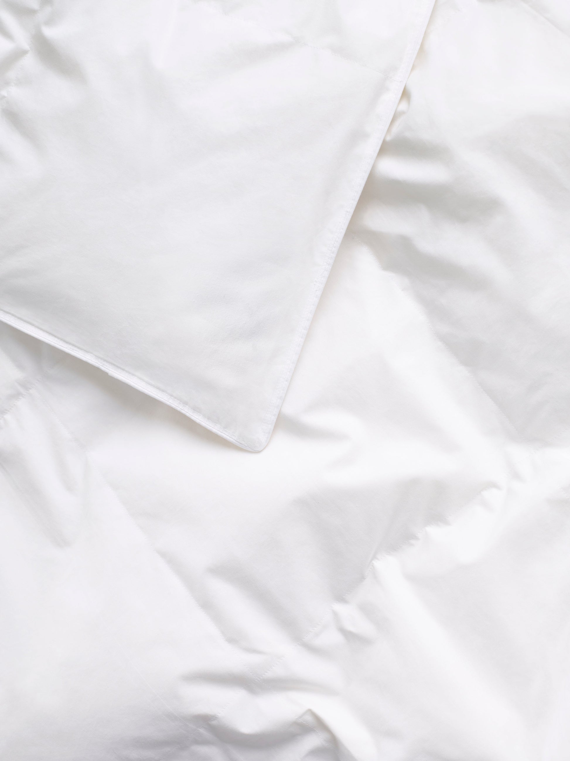 Close-up of the corner of a white sheet, visible on top of a high-quality duvet.