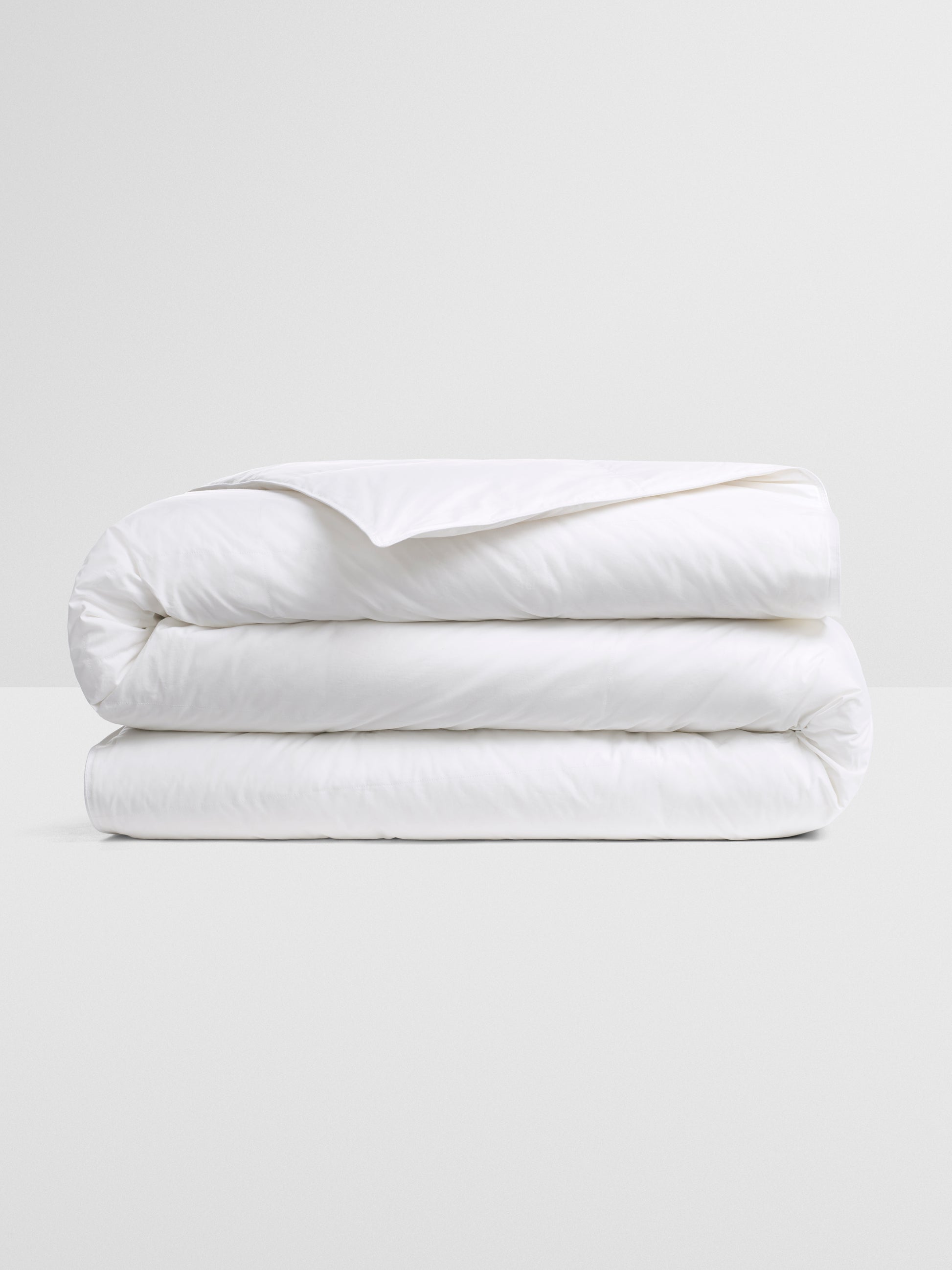 A folded white down duvet on a white background.