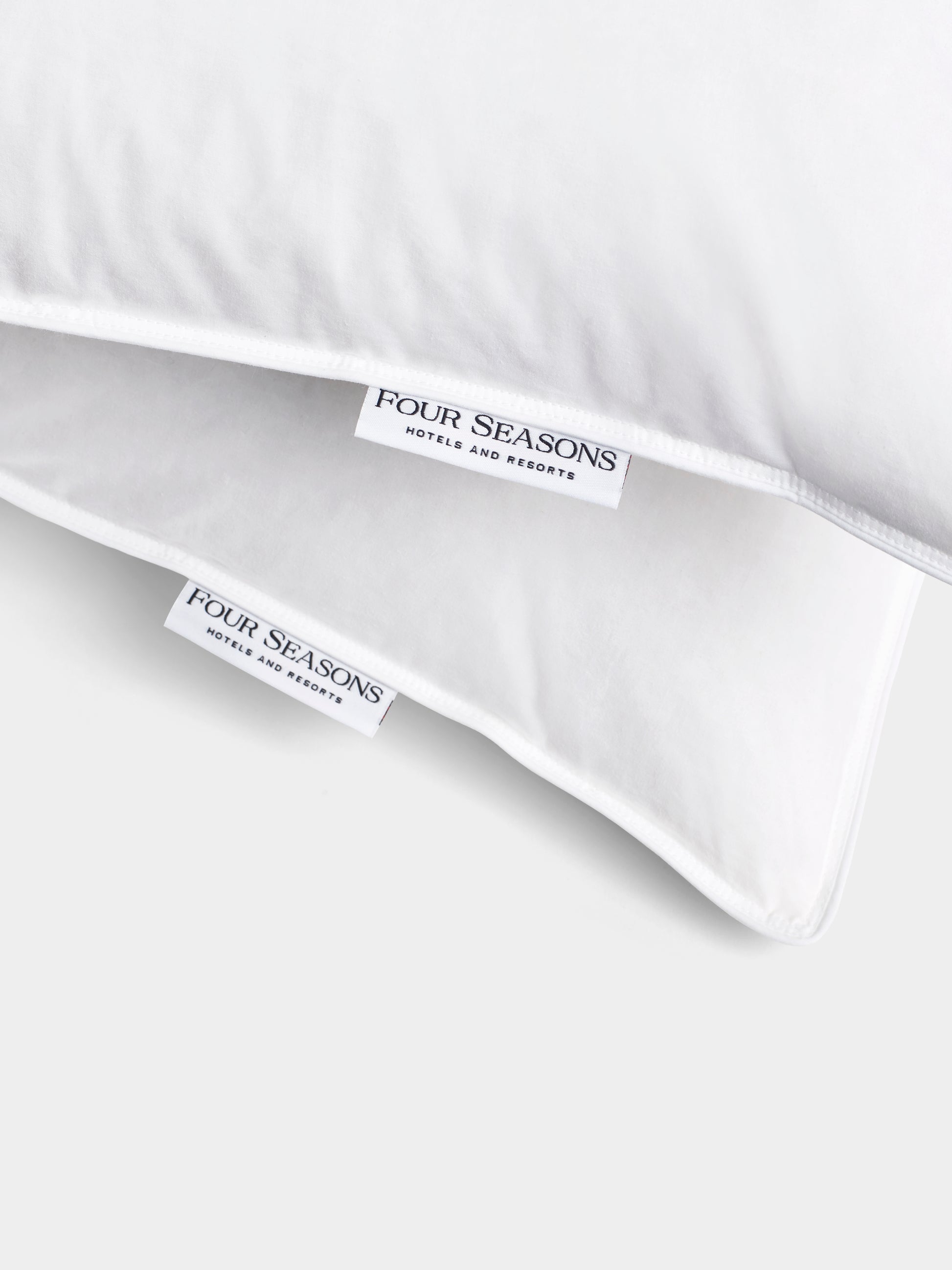 Close-up of two white labels sewn into a duvet cover. Both labels feature the Four Seasons Hotels and Resorts logo.