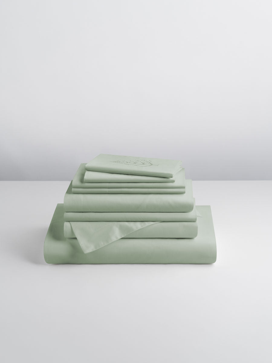 A set of Florentine Sage-colored sheets, folded into perfect rectangles and stacked on a flat surface.