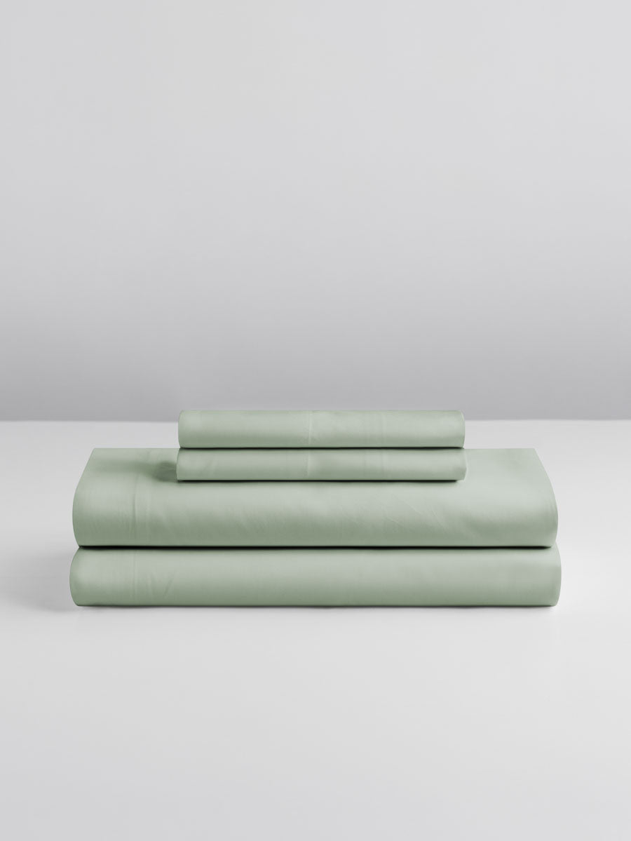 A set of Florentine Sage-colored sheets, folded into perfect rectangles and stacked on a flat surface.