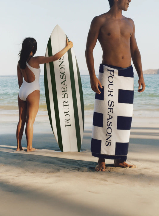 Two people on a beach with surfboards and towels branded 'Four Seasons'.