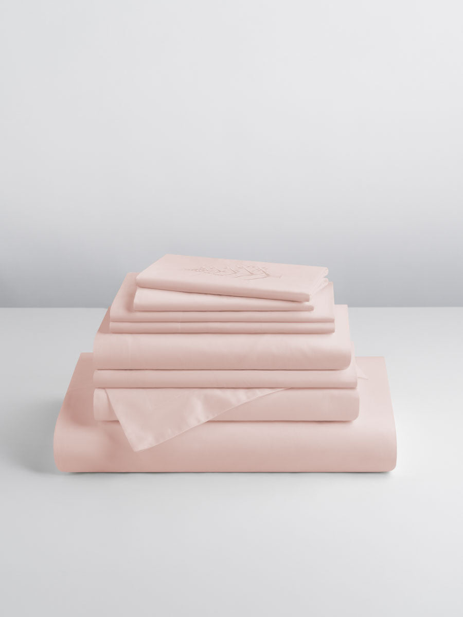 A set of Kyoto Blush-colored sheets, folded into perfect rectangles and stacked on a flat surface.