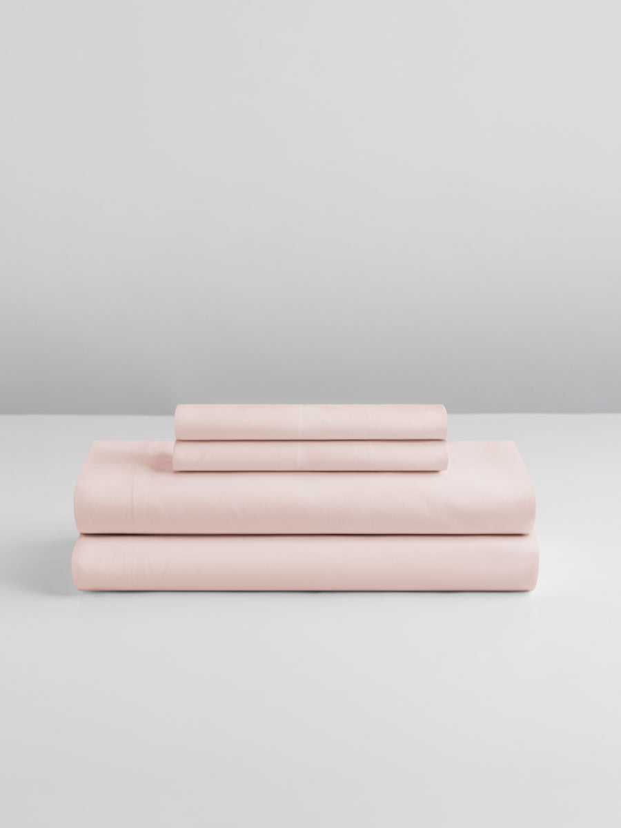 A set of Kyoto Blush-colored sheets, folded into perfect rectangles and stacked on a flat surface.