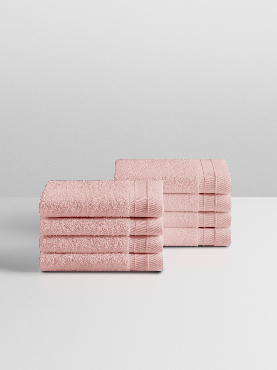 A stack of eight soft, “Kyoto Blush” colored clothes neatly folded on a white surface.