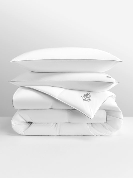 White pure down duvet bedding with a pure down pillows stacked on top with a Four Seasons Logo on a light grey background.