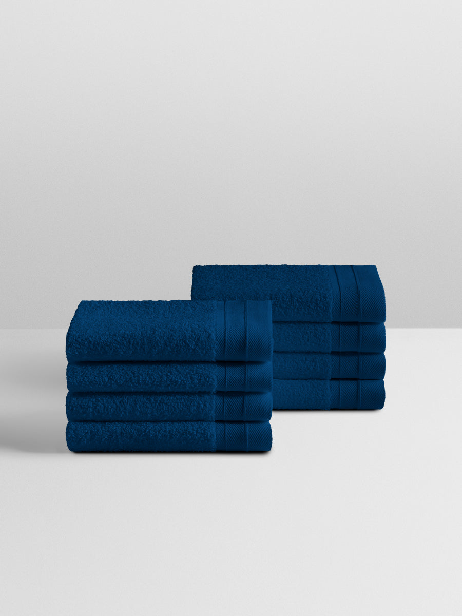 A stack of eight soft, “Riviera Navy” colored bath wash cloth neatly folded on a white surface. - {{Riviera Navy}}