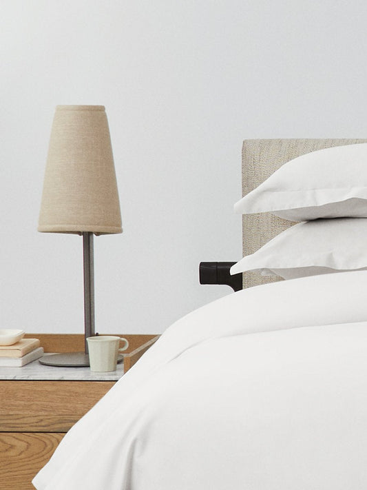 Bed dressed with a duvet in Signature White color and two pillows with embroidery along the edge. - {{Signature White}}