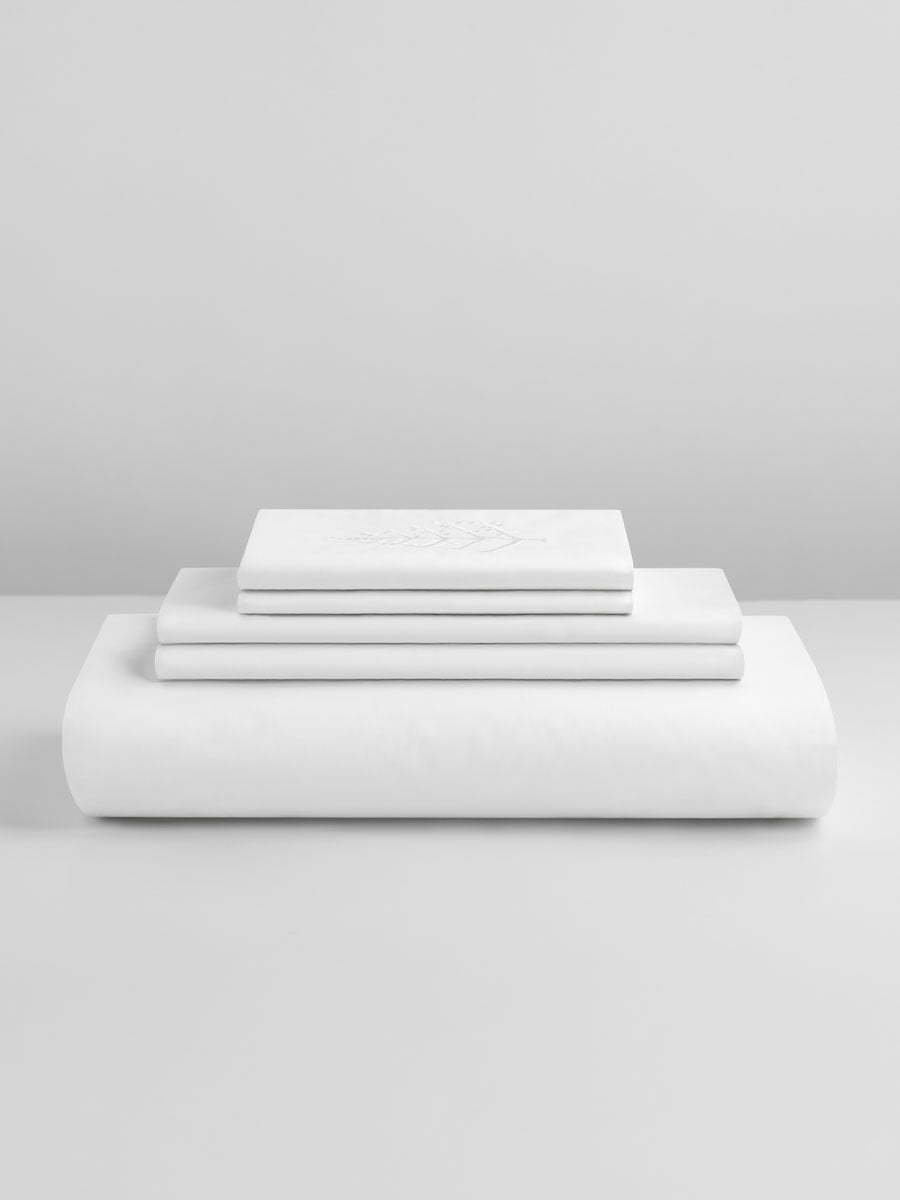 A bed covered with a Signature White-colored duvet and several pillows delicately stacked.