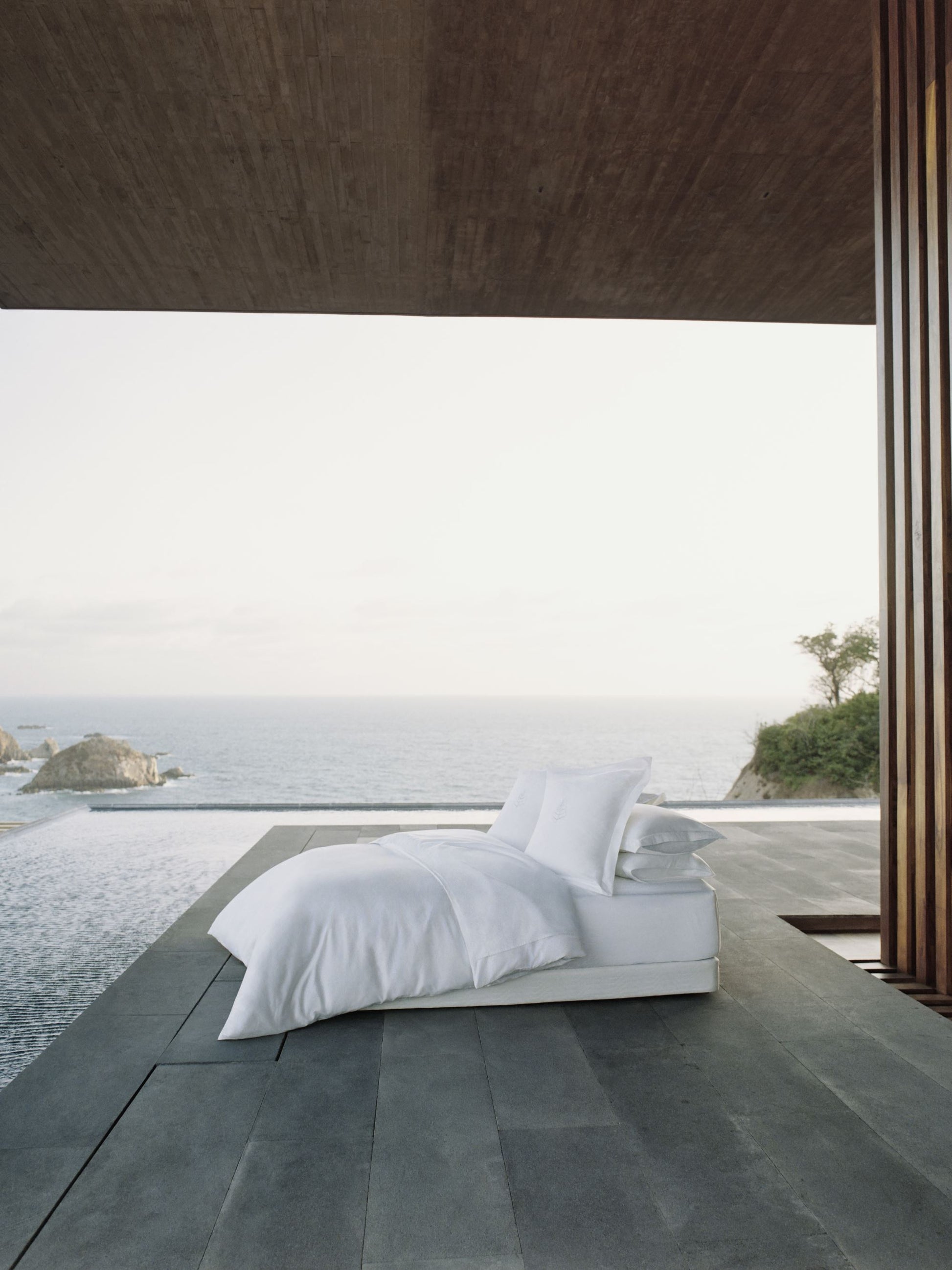 Minimalist design bed with white sheets and carefully arranged pillows, overlooking the sea.