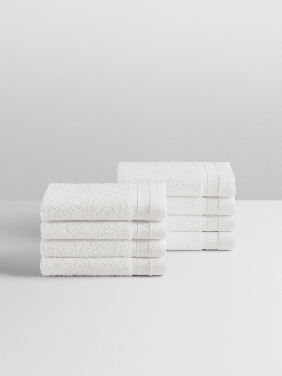 A stack of eight soft, “Signature White” colored bath wash clothes neatly folded on a white surface.