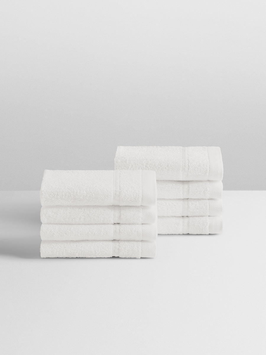 A stack of eight soft, “Signature White” colored bath wash cloths neatly folded on a white surface.