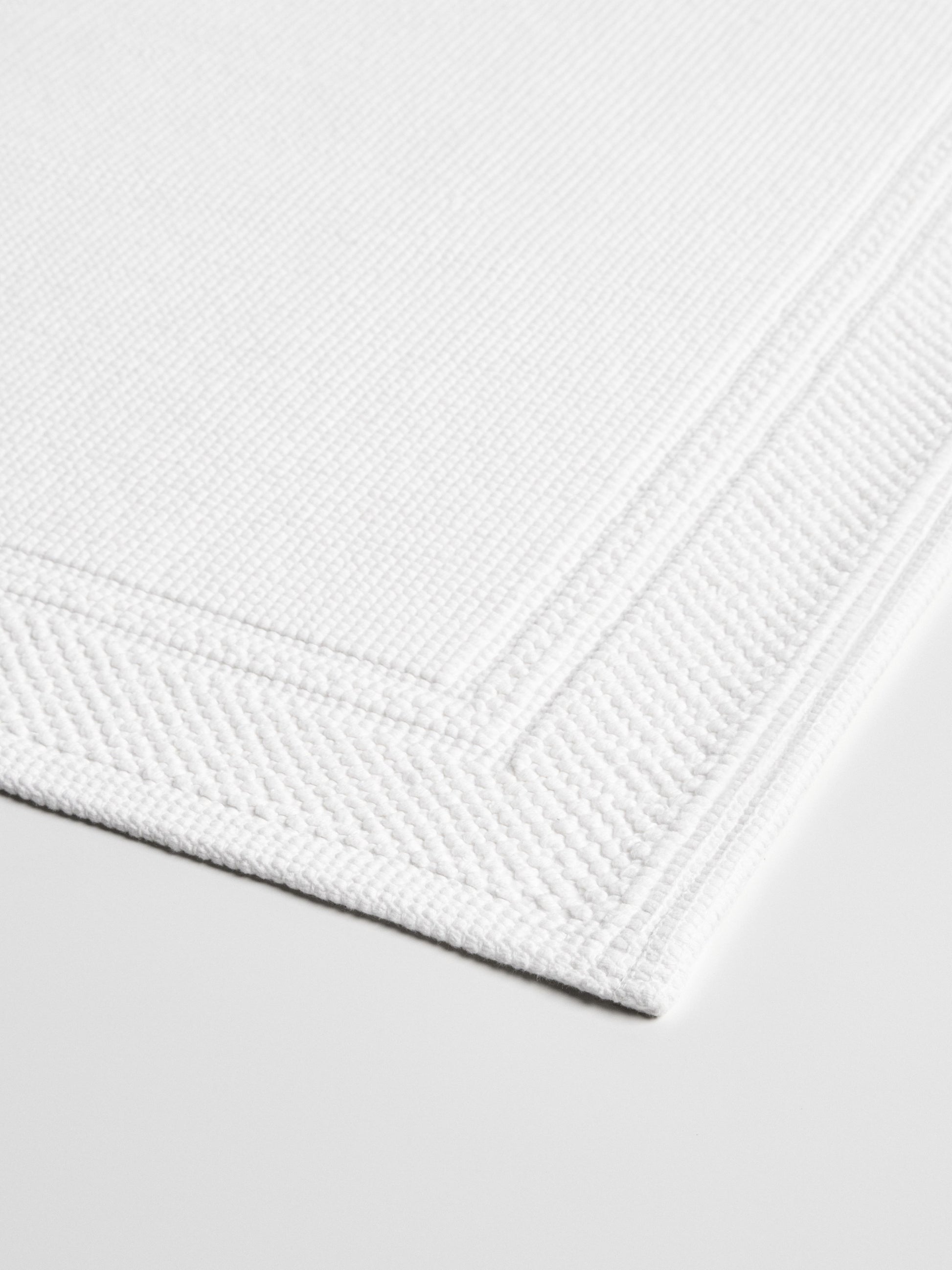 Close-up of a white bath mat with a textured surface and a subtle border.