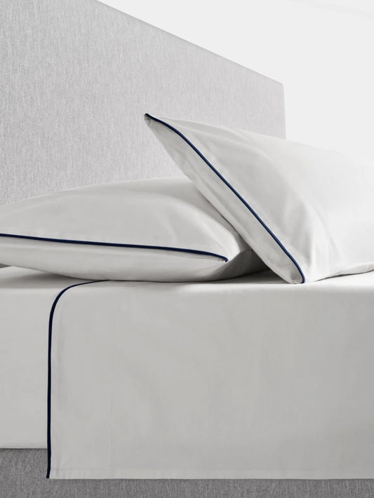 Sycamore Sheet Set in Signature White —flat and fitted sheet with modern piped hem, styled on bed with matching pillowcases. - {{Signature White}}