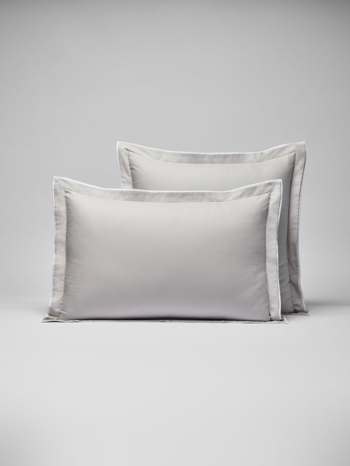 Two pillows with a woven border around them, one placed behind the other. - {{Turkish Silver/Signature White}}