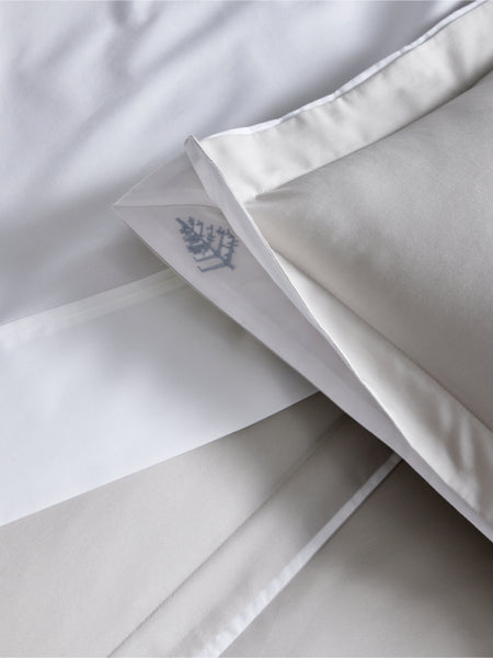 Close-up of a white pillowcase with a subtle pattern of the Four Seasons logo. The fabric is soft and luxurious.