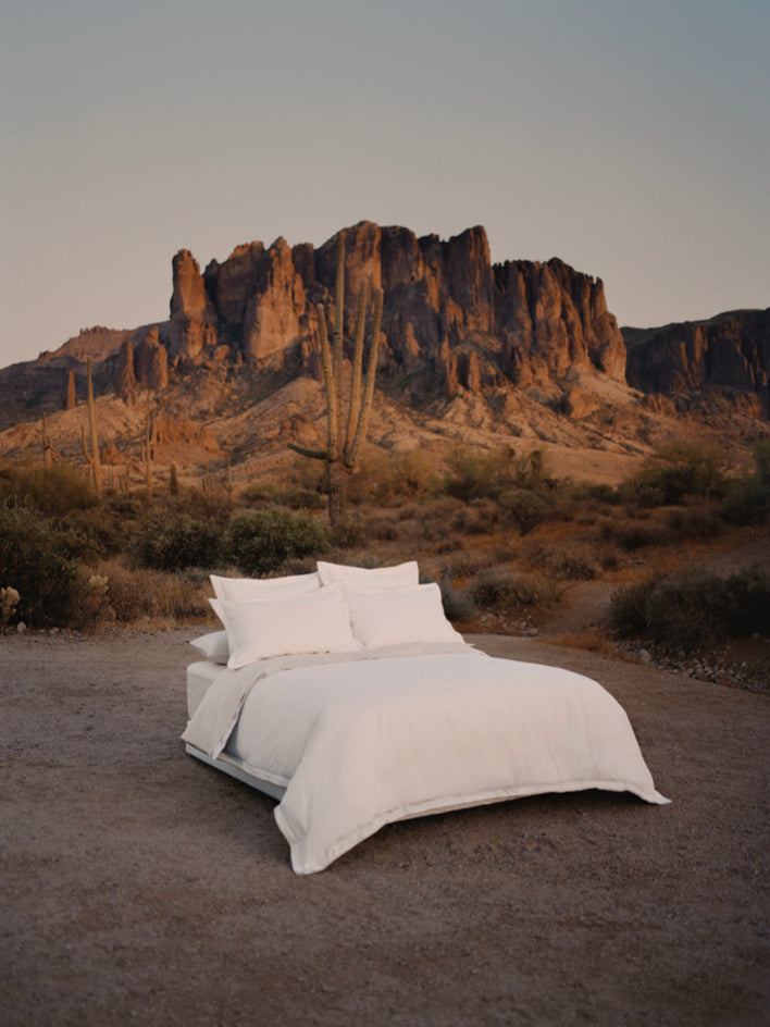 Bed dressed with white sheets and a duvet, with several pillows carefully arranged.