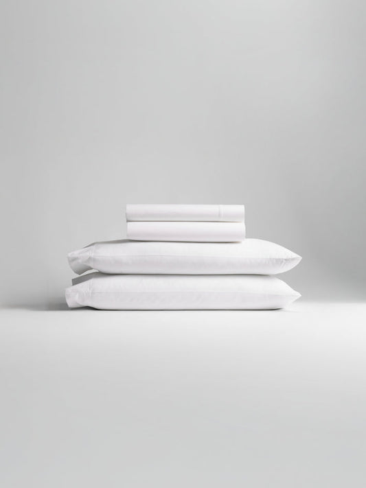 A stack of bedding, including pillowcases and sheets in Signature White color. - {{Signature White}}