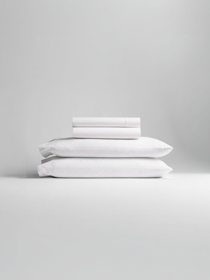 A stack of white and light gray bedding, including pillowcases and sheets.