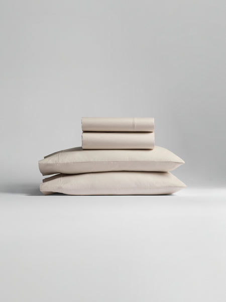 A stack of bedding, including pillowcases and sheets in Balinese Pearl color.