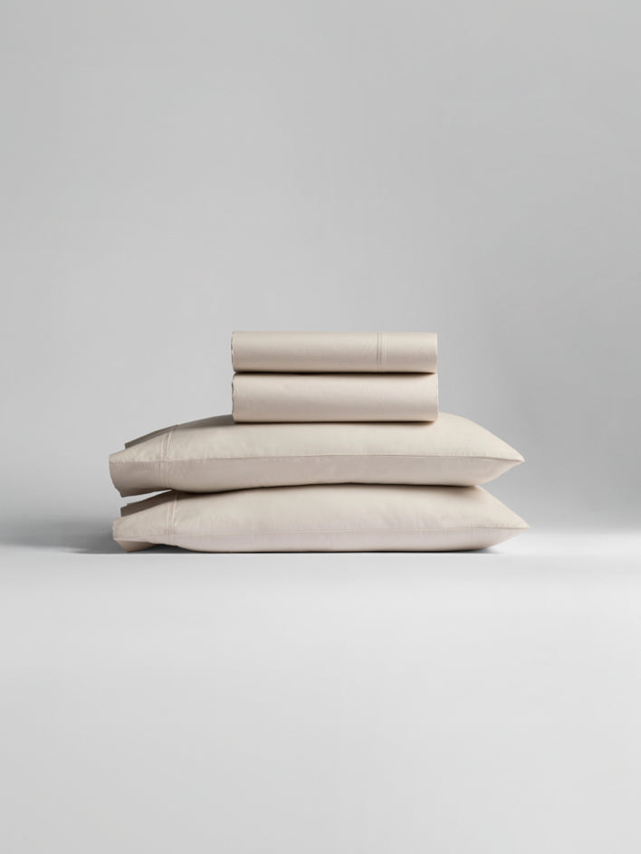 A stack of white and light gray bedding, including pillowcases and sheets.